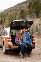 Portrait of young couple sitting in car trunk in non-urban scene