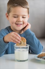 Boy (4-5) dipping cookie in milk.