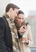 Couple in winter clothes looking at phone.
