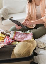 Woman using digital tablet while packing suitcase.