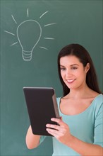 Woman using digital tablet in front of blackboard.
