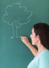 Woman drawing tree on blackboard.