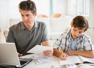 Father working on laptop and son (8-9) doing homework