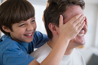 Son (8-9) covering father's eyes