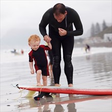 Father and his son (2-3) on beach by surfboard