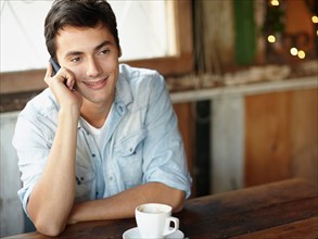 Young man sitting in cafe and talking on cell phone