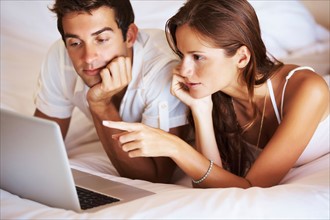 Couple using laptop while lying in bed