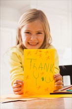 Girl (6-7) holding drawing with text 'thank you'