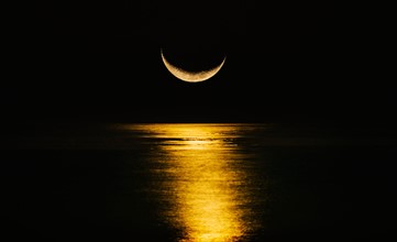Crescent moon reflecting in sea.