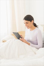 Woman sitting in bed and using digital tablet.