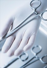 Close up of hand in surgical glove holding dental forceps, studio shot.