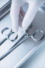 Close up of hand in surgical glove choosing dental forceps, studio shot.