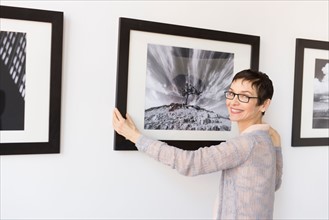 Woman hanging photographs in art gallery.