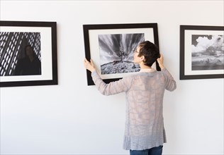 Woman hanging photographs in art gallery.