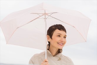 Portrait of smiling woman wearing raincoat and holding umbrella.