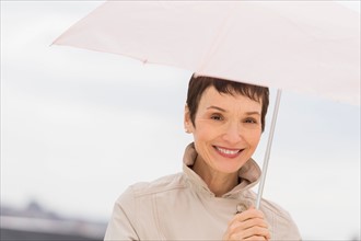Portrait of smiling woman wearing raincoat and holding umbrella.