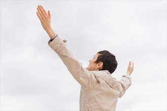 Woman in raincoat raising arms up into cloudy sky.
