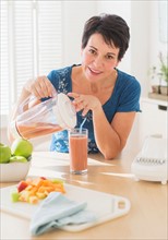 Portrait of mature woman pouring glass of smoothie from blender