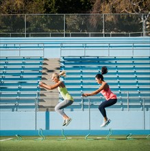 Two women jumping over hurdles