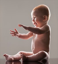 Studio shot of naked baby boy (18-23 months) sitting and gesturing