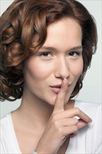 Studio shot portrait of young woman in white blouse with finger on lips