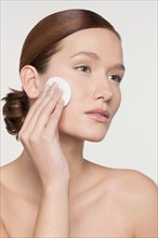 Studio shot portrait of young woman purifying her face with cotton pad