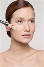Studio shot of young woman applying foundation on face