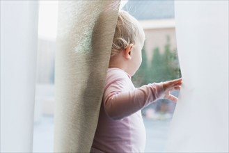 Baby girl (12-17 months) looking through window