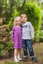 Brother (6-7) and sister (4-5) posing together in garden