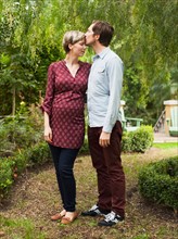 Pregnant couple embracing and kissing in garden