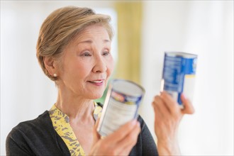 Senior woman reading labels on canned food.
