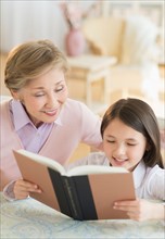 Granddaughter (8-9) and grandmother reading book.