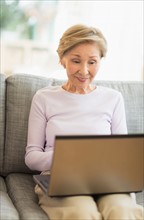 Senior woman sitting on sofa and using laptop.