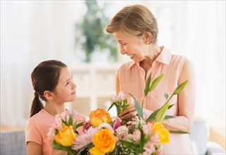 Granddaughter (8-9) and grandmother arranging flowers at home.