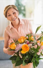 Senior woman arranging flowers in living room.