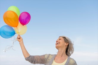 Senior woman holding bunch of colorful balloons.