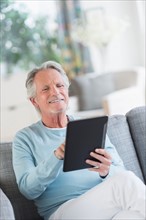 Senior man sitting on sofa with digital tablet.