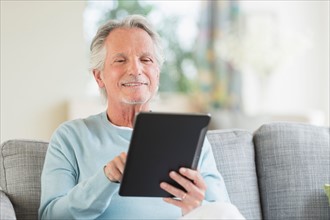 Senior man sitting on sofa with digital tablet.