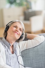 Senior woman sitting on sofa and listening to music.