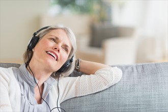 Senior woman sitting on sofa and listening to music.