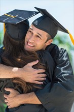 Male and female students embracing on graduation ceremony.