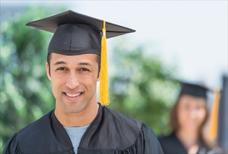 Portrait of male student on graduation ceremony with female student in background.