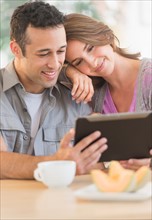 Young couple using digital tablet at kitchen table.