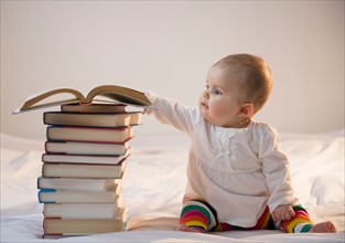 Baby girl (6-11 months) sitting in bed with stack of books
