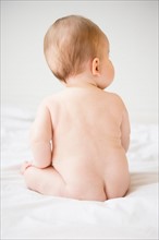 Rear view of naked baby girl (6-11 months) sitting on bed