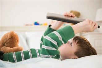 Boy (4-5) lying down on bed and holding digital tablet