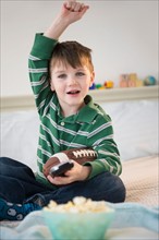 Portrait of cheerful boy (4-5) sitting on bed, holding football