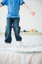 Low section of boy (4-5) jumping on bed