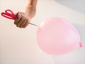 Close up of woman's hand popping balloon with scissors