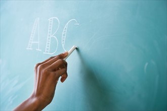 Close up of woman's hand writing alphabet on blackboard